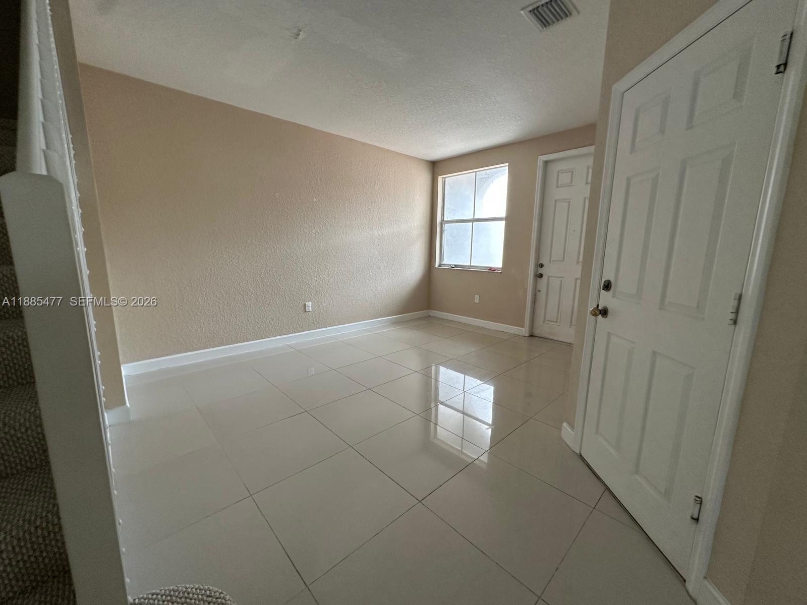 An empty room features beige walls, white trim, and large, glossy light-colored floor tiles — 1026 NE 207th Ter # 1026, Miami FL 33179, MIAMI, FL