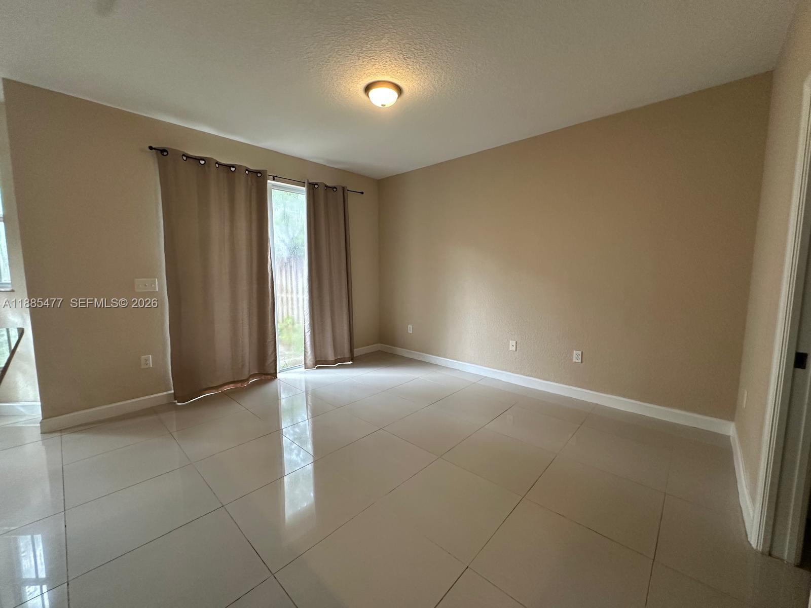 An empty room features beige walls, large light-colored floor tiles, and a sliding glass door — 1026 NE 207th Ter # 1026, Miami FL 33179, MIAMI, FL