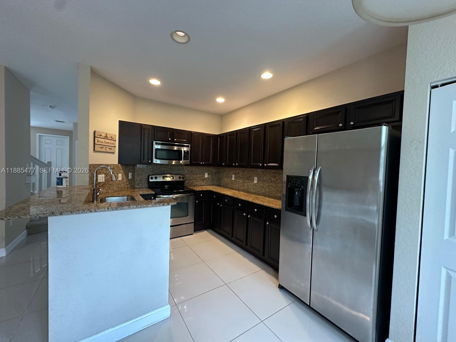 A kitchen features dark wood cabinets, granite countertops, stainless steel appliances, and white tile flooring — 1026 NE 207th Ter # 1026, Miami FL 33179, MIAMI, FL