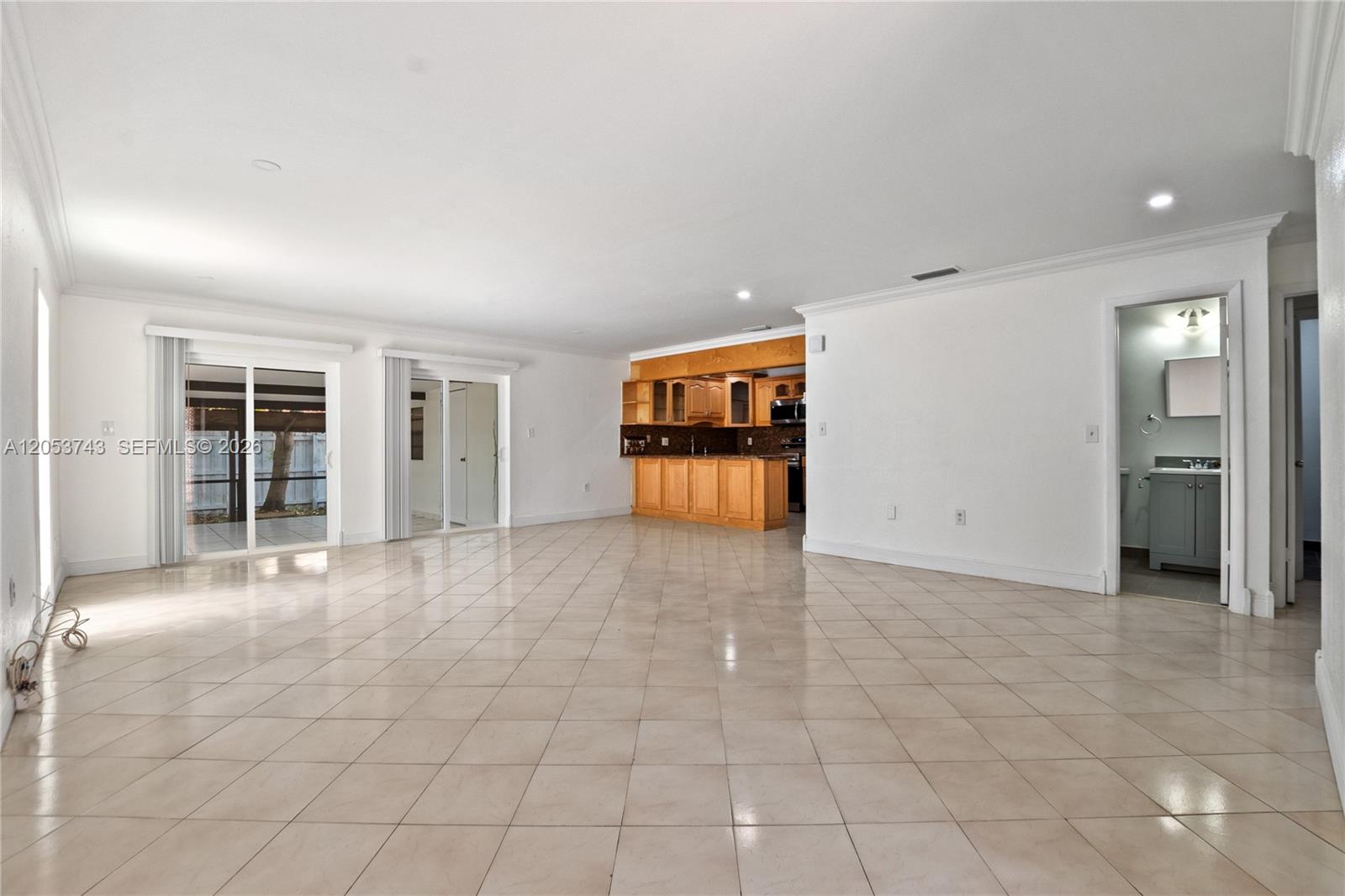 A spacious room with light tile flooring, white walls, sliding glass doors, and a kitchen — 12262 SW 10th St, Miami FL 33184, MIAMI, FL