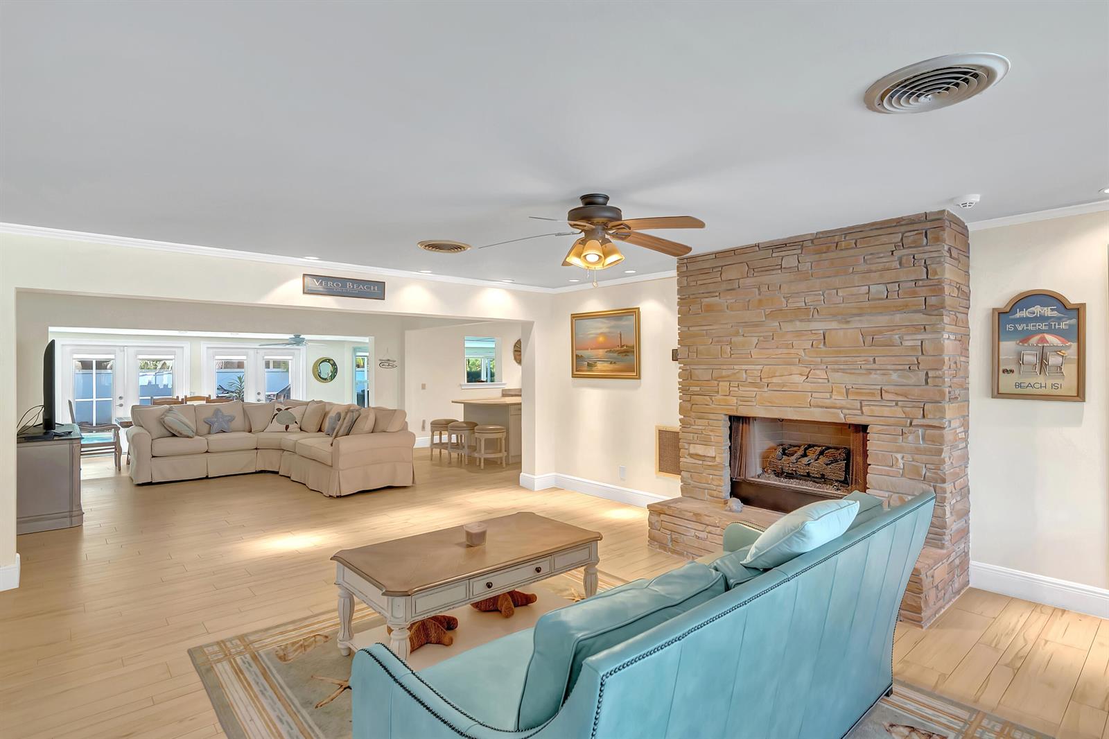 A living room features a stone fireplace, a teal sofa, and light wood flooring — 500 Gardenia Lane, Vero Beach FL 32963, VERO BEACH, FL