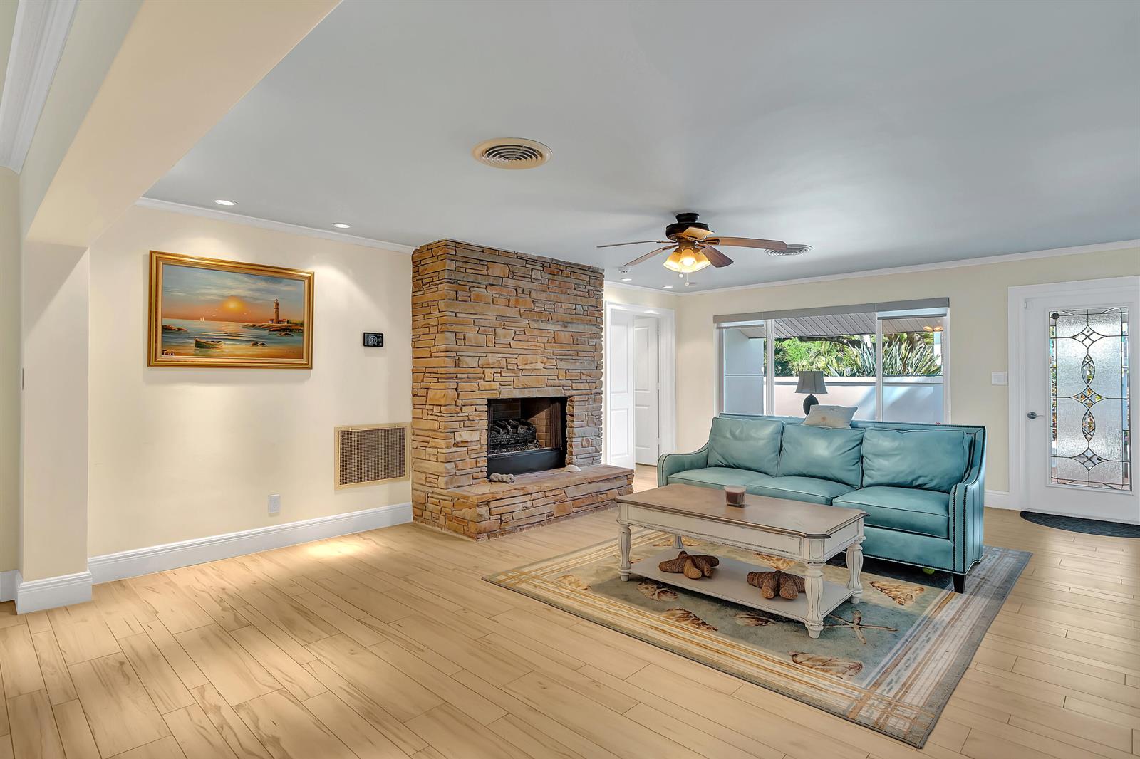 A living room features a stone fireplace, light wood flooring, and a teal leather sofa — 500 Gardenia Lane, Vero Beach FL 32963, VERO BEACH, FL
