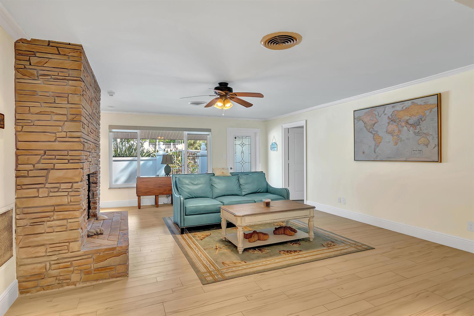 A living room features a stone fireplace, a teal sofa, and a world map wall hanging — 500 Gardenia Lane, Vero Beach FL 32963, VERO BEACH, FL