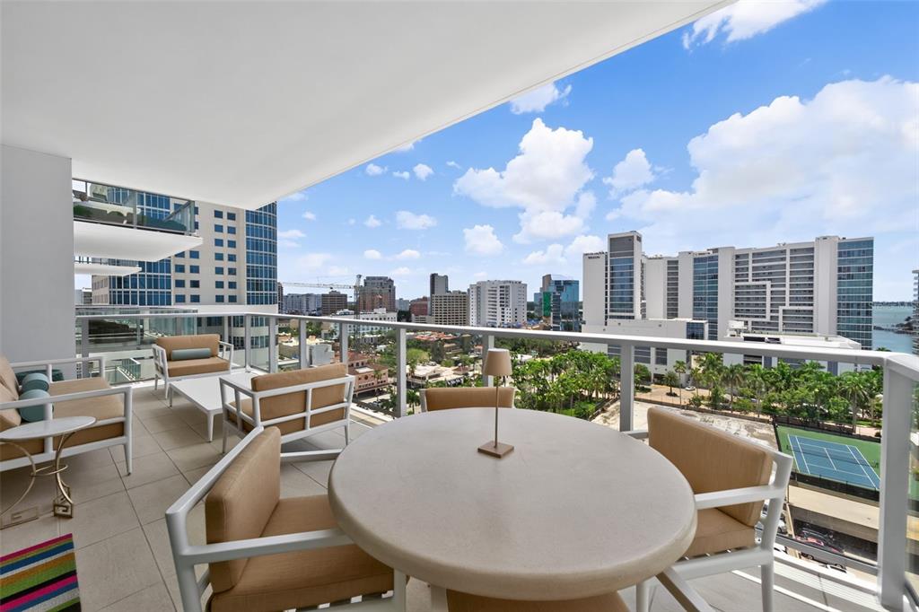 A balcony with outdoor furniture overlooks a city skyline and a tennis court — 301 QUAY COMMONS UNIT 1009, SARASOTA, FL