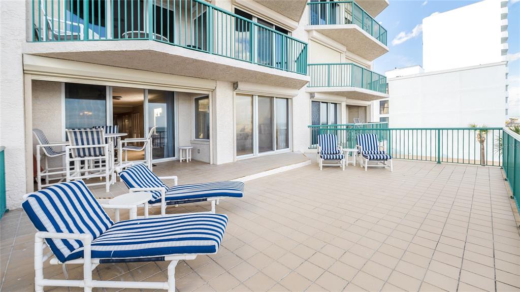 A large outdoor balcony features tiled flooring, blue and white striped lounge chairs, and railings — 3311 S ATLANTIC AVENUE UNIT 202, DAYTONA BEACH, FL