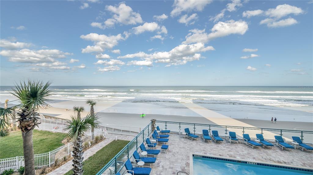 An elevated view of a beachside swimming pool deck with lounge chairs and ocean waves — 3311 S ATLANTIC AVENUE UNIT 202, DAYTONA BEACH, FL