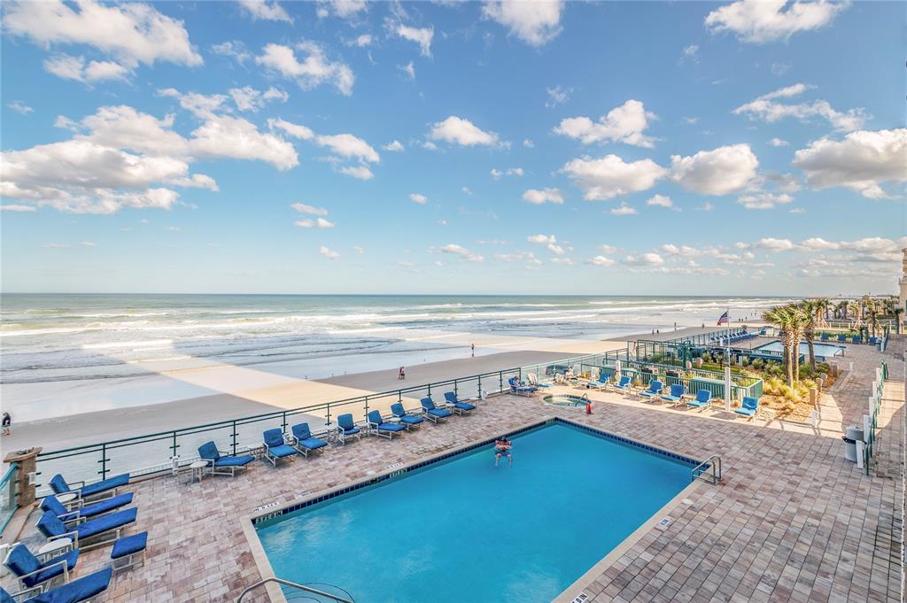 An elevated view of a swimming pool and patio overlooking a sandy beach and ocean — 3311 S ATLANTIC AVENUE UNIT 202, DAYTONA BEACH, FL