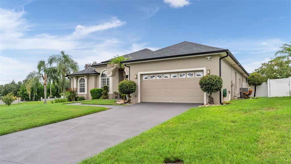 A tan single-story house with a two-car garage, a paved driveway, and palm trees — 6726 HARTSWORTH DRIVE, LAKELAND, FL