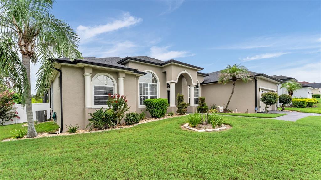 A single-story suburban house with a tan stucco exterior, arched windows, and a palm tree — 6726 HARTSWORTH DRIVE, LAKELAND, FL