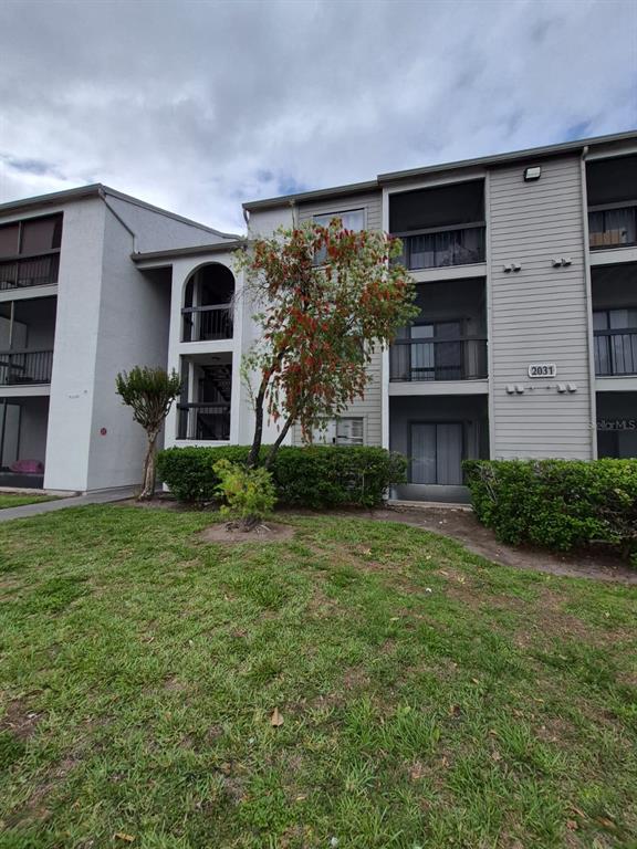 A multi-story apartment building with beige siding, balconies, and a small tree in front — 2031 CASCADES BOULEVARD UNIT 307, KISSIMMEE, FL