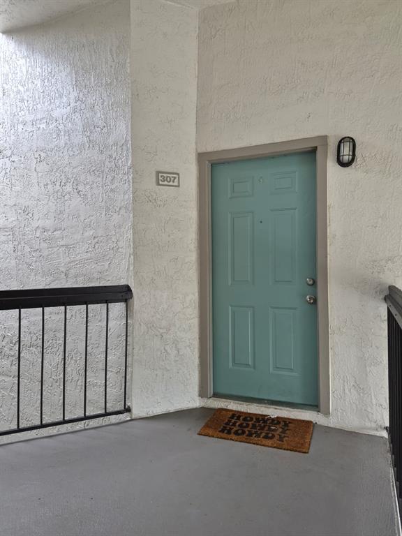 A teal apartment door with a "Howdy" doormat is located on an outdoor balcony — 2031 CASCADES BOULEVARD UNIT 307, KISSIMMEE, FL