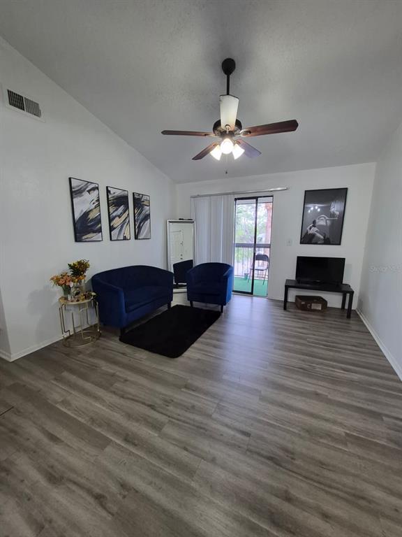 A living room features a blue sofa, a matching armchair, and wood-look laminate flooring — 2031 CASCADES BOULEVARD UNIT 307, KISSIMMEE, FL