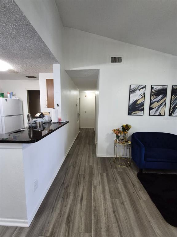 A kitchen with a black countertop overlooks a hallway and a living area with flooring — 2031 CASCADES BOULEVARD UNIT 307, KISSIMMEE, FL