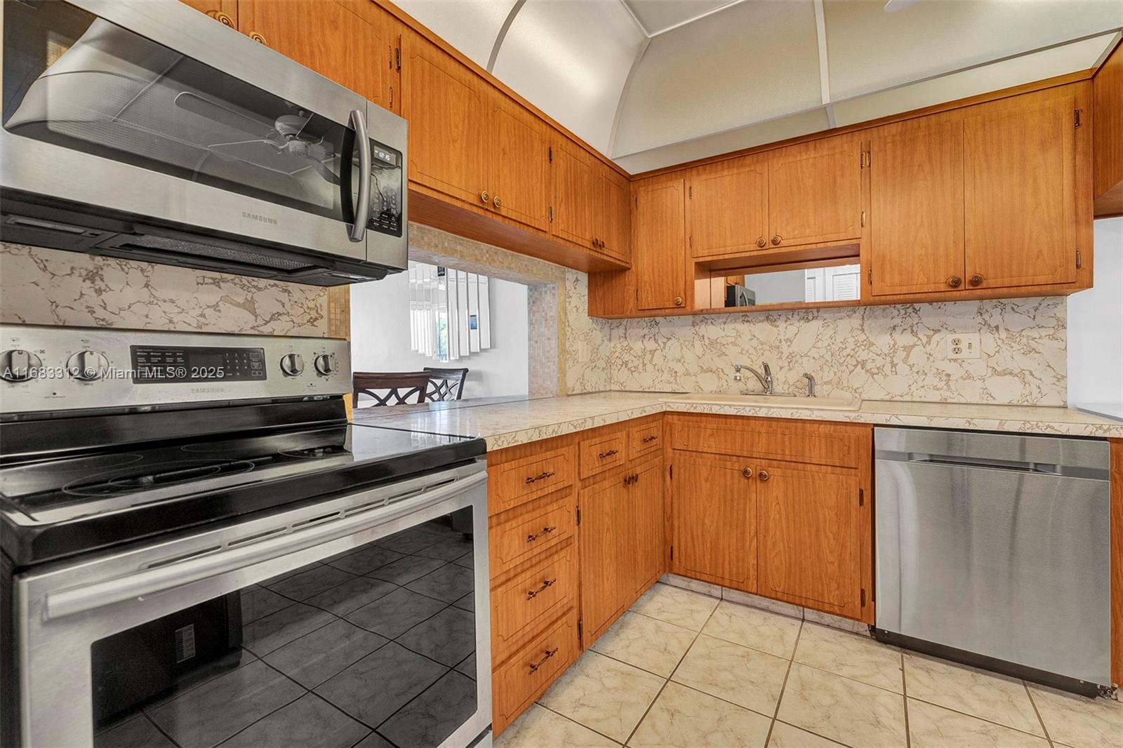 A kitchen features wood cabinets, stainless steel appliances, a pass-through window, and tiled flooring — 330 SE 2nd St # 303F, Hallandale Beach FL 33009, HALLANDALE BEACH, FL