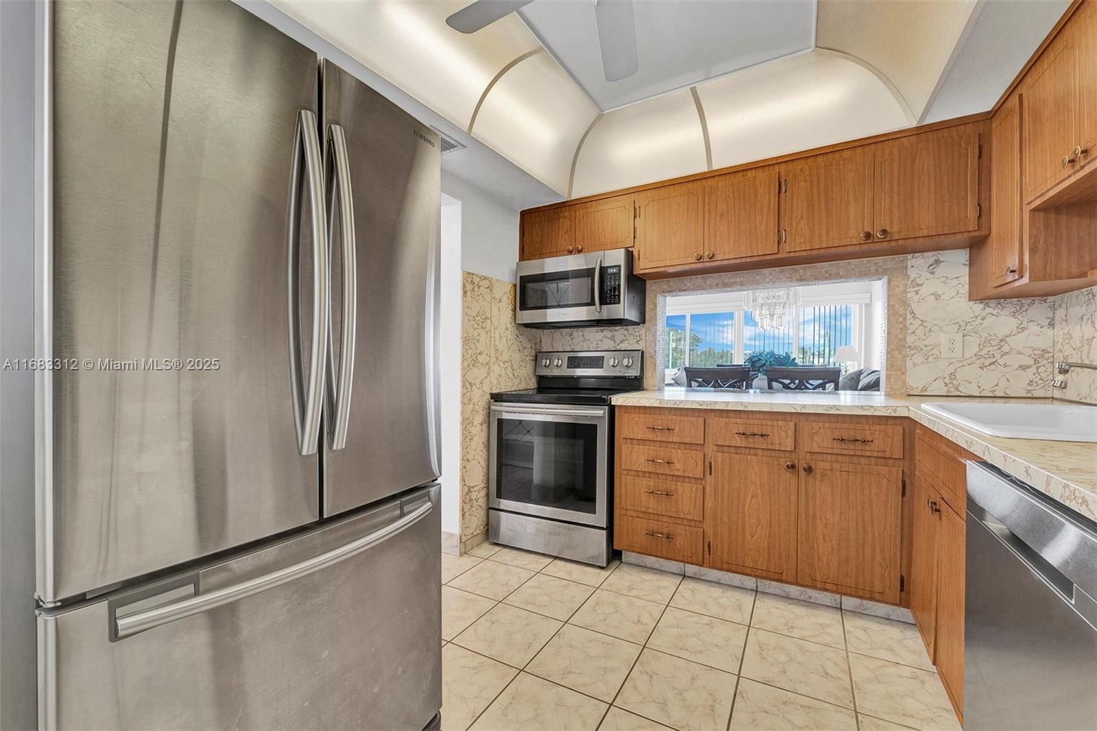 A kitchen features stainless steel appliances, wood cabinets, tiled floors, and a pass-through window — 330 SE 2nd St # 303F, Hallandale Beach FL 33009, HALLANDALE BEACH, FL