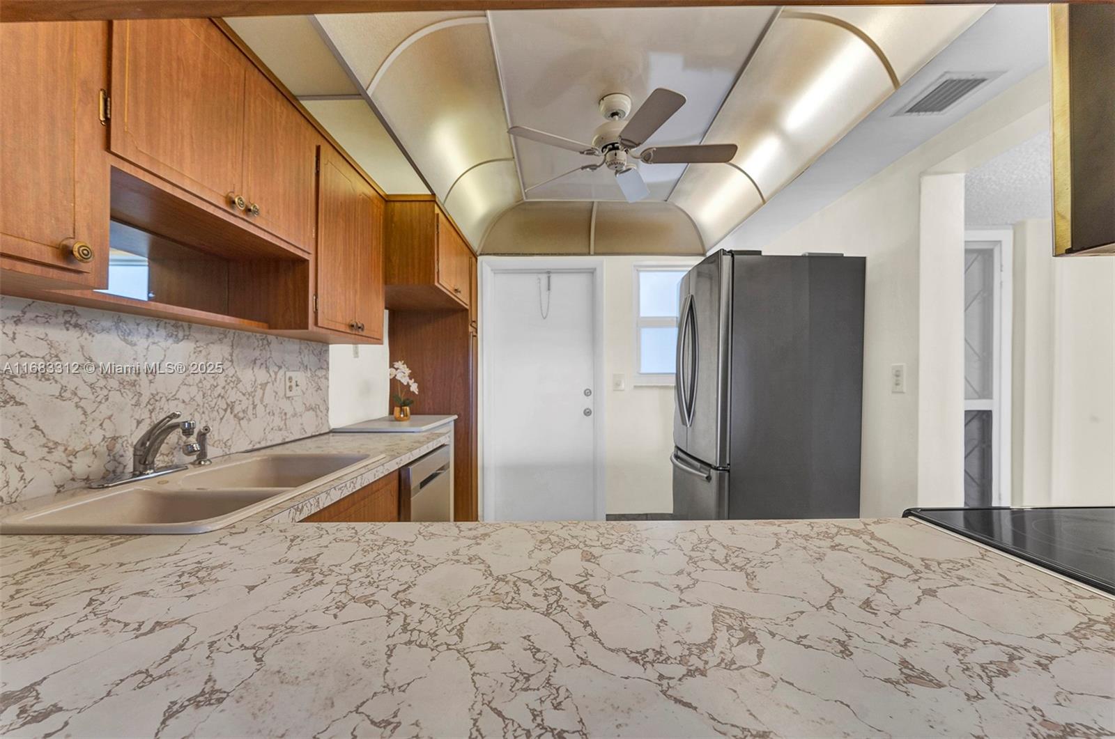 A kitchen features wood cabinets, marble-patterned countertops, a stainless steel refrigerator, and a ceiling fan — 330 SE 2nd St # 303F, Hallandale Beach FL 33009, HALLANDALE BEACH, FL