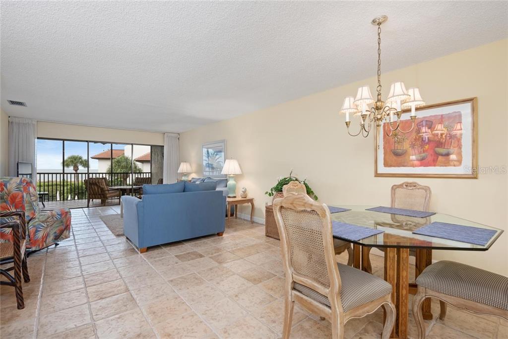A dining area and living room with tile floors, a glass table, and a balcony view — 5393 GULF OF MEXICO DRIVE UNIT 208, LONGBOAT KEY, FL