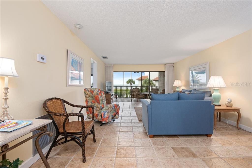 A living room with tile floors, a blue sofa, a patterned armchair, and a balcony — 5393 GULF OF MEXICO DRIVE UNIT 208, LONGBOAT KEY, FL