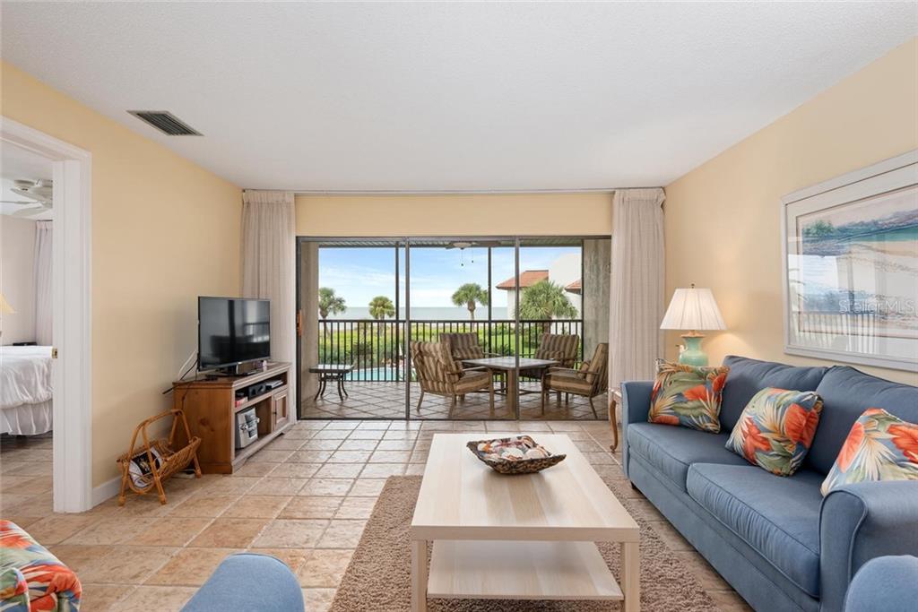 A living room with tile floors, a blue sofa, and a balcony overlooking the ocean — 5393 GULF OF MEXICO DRIVE UNIT 208, LONGBOAT KEY, FL