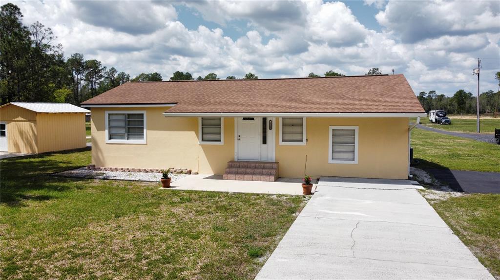 A single-story yellow house with a brown roof, a concrete driveway, and a small shed — 2305 STATE ROAD 33 HIGHWAY, CLERMONT, FL
