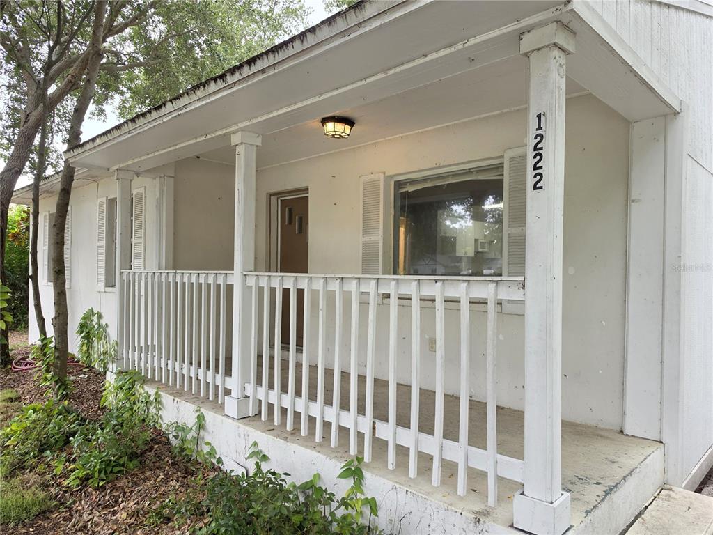 A white house exterior features a covered front porch with a wooden railing and columns — 1222 ELDRIDGE STREET, CLEARWATER, FL