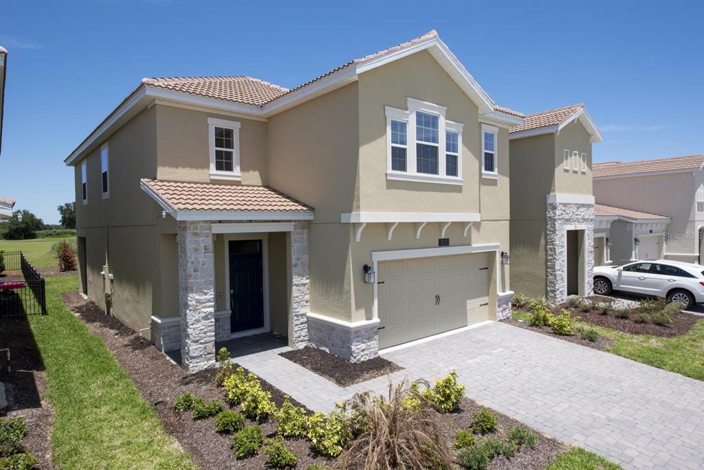 A two-story house with a tan stucco exterior, stone accents, and a paved driveway — 1037 BLACKWOLF RUN ROAD, DAVENPORT, FL