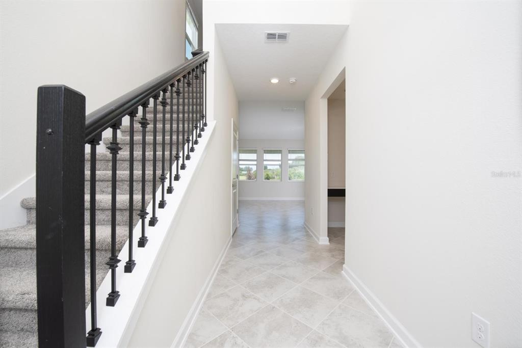 A hallway with tile flooring leads to a living area with windows and a staircase — 1037 BLACKWOLF RUN ROAD, DAVENPORT, FL