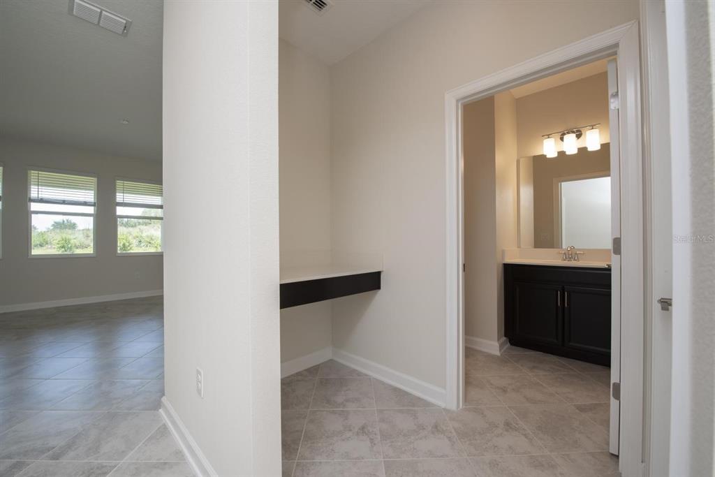 A hallway with a built-in desk leads into a bathroom with a dark wood vanity — 1037 BLACKWOLF RUN ROAD, DAVENPORT, FL