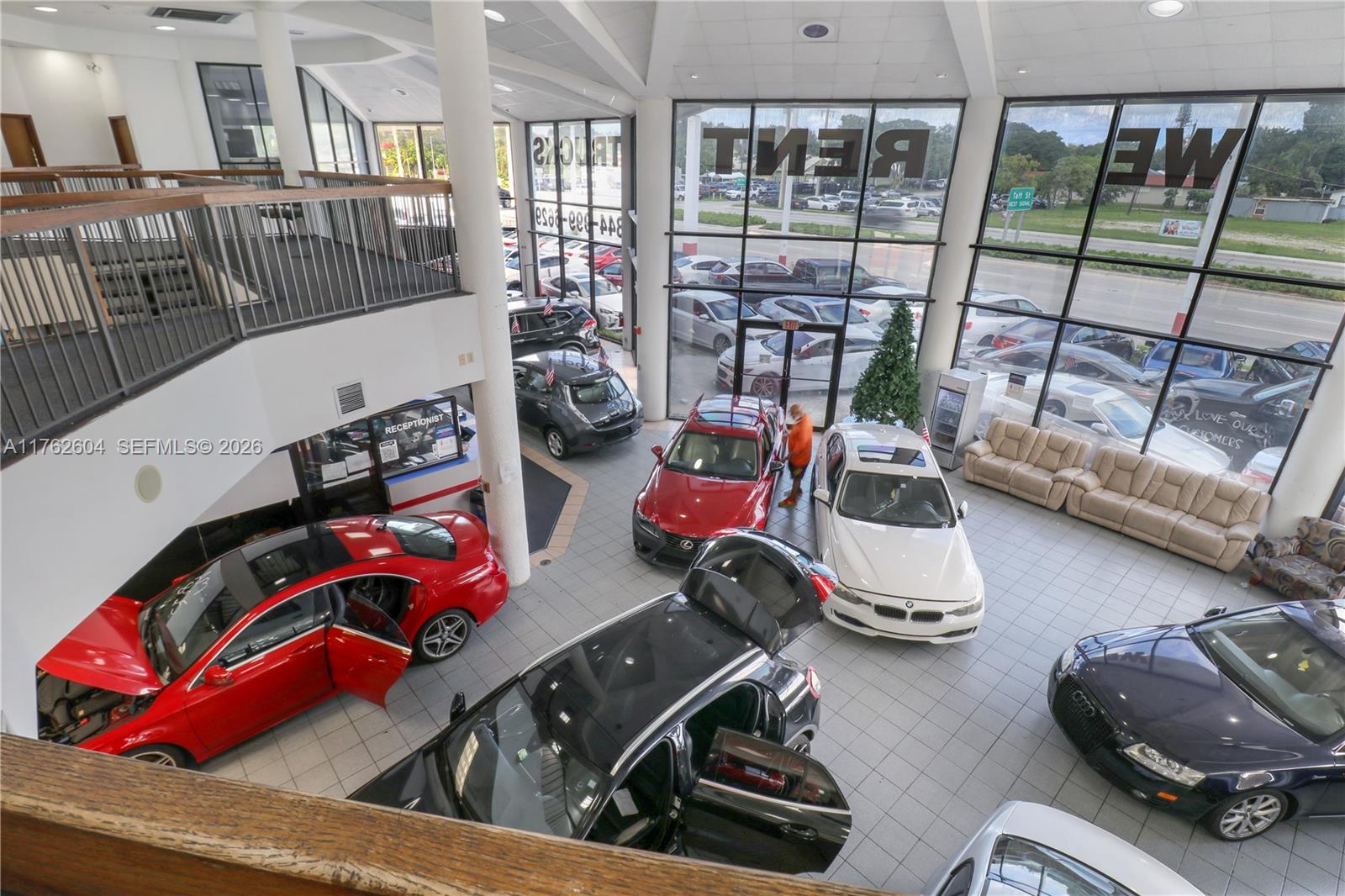 An elevated view of a car dealership showroom featuring multiple vehicles and a reception desk — 1450 N State Road 7, Hollywood FL 33021, HOLLYWOOD, FL