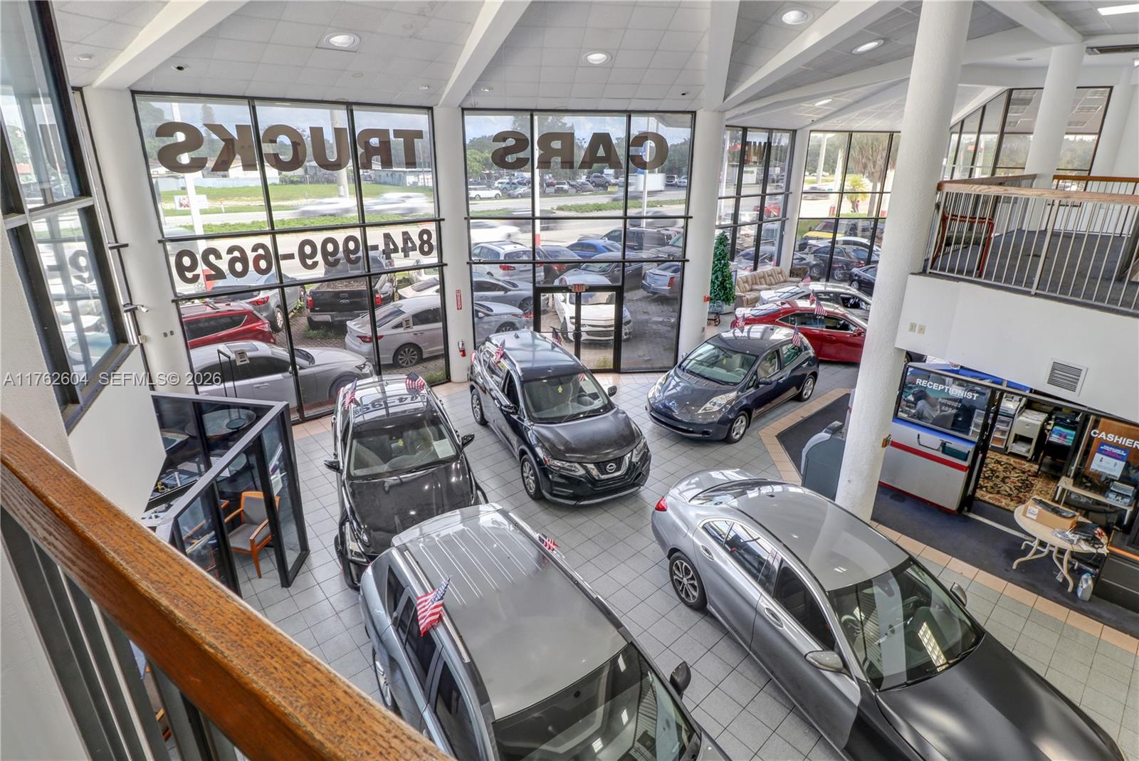 An elevated view of a car dealership showroom featuring multiple vehicles on a tiled floor — 1450 N State Road 7, Hollywood FL 33021, HOLLYWOOD, FL