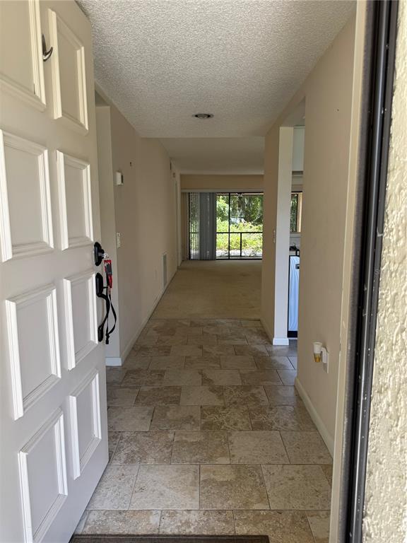 An entryway with stone tile flooring leads into a carpeted living area with a sliding door — 4767 WINSLOW BEACON UNIT 25, SARASOTA, FL