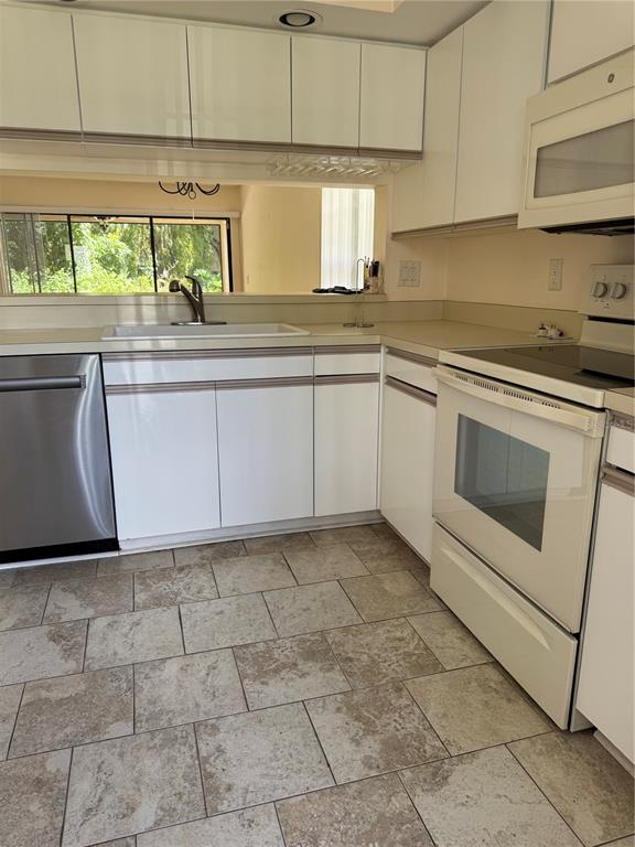 A kitchen features white cabinetry, a stainless steel dishwasher, a white stove, and tiled flooring — 4767 WINSLOW BEACON UNIT 25, SARASOTA, FL