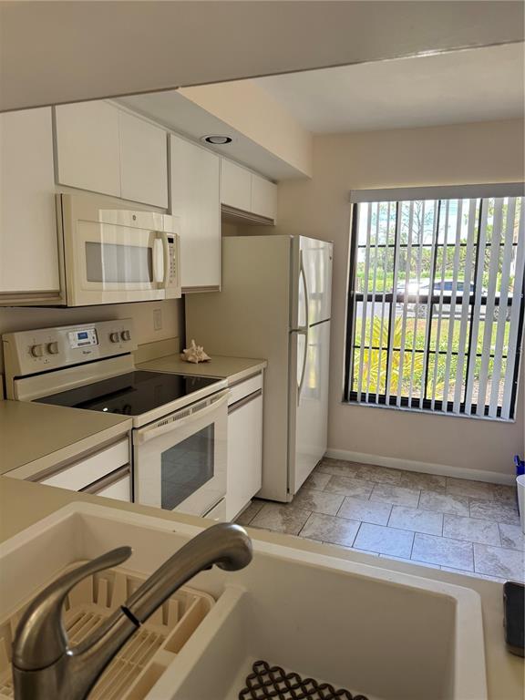 A kitchen features white cabinetry, a white refrigerator, a stove, and a window with blinds — 4767 WINSLOW BEACON UNIT 25, SARASOTA, FL
