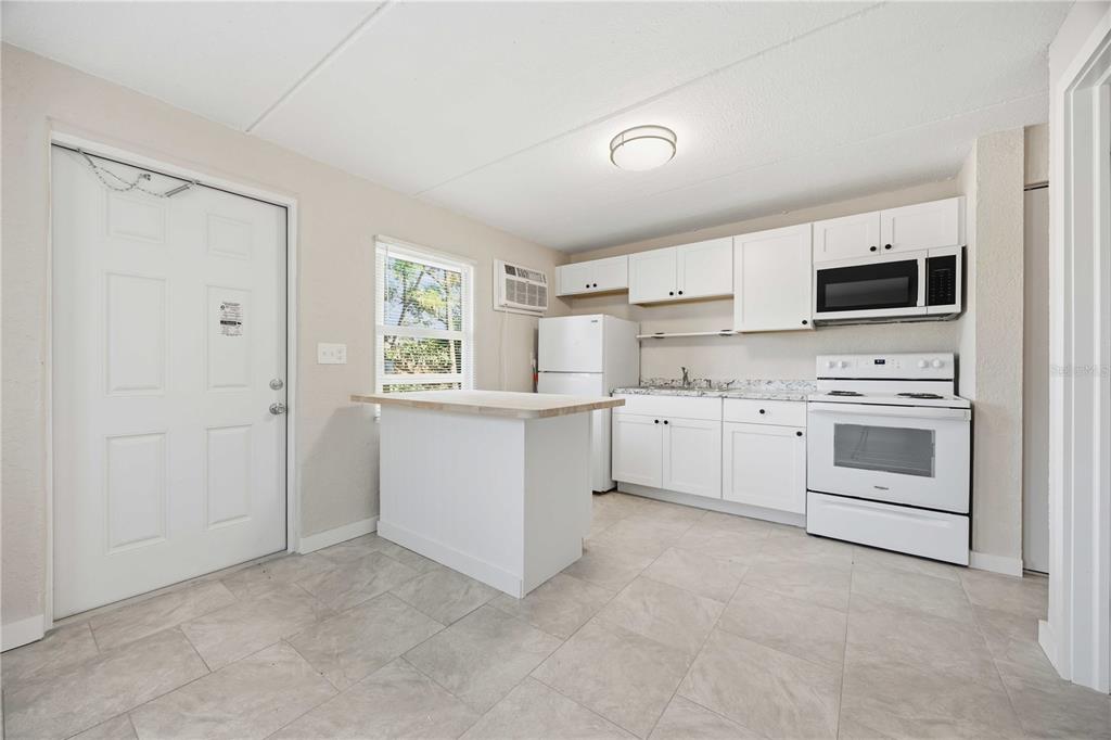A kitchen features white cabinets, white appliances, a small island, and light-colored tile flooring — 419 GRAPEFRUIT AVENUE UNIT 2A, SEBRING, FL