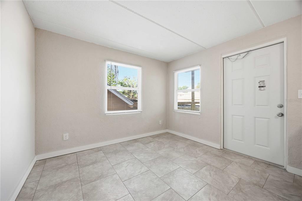 An empty room with light-colored tile flooring, two windows, and a white exterior door — 419 GRAPEFRUIT AVENUE UNIT 2A, SEBRING, FL
