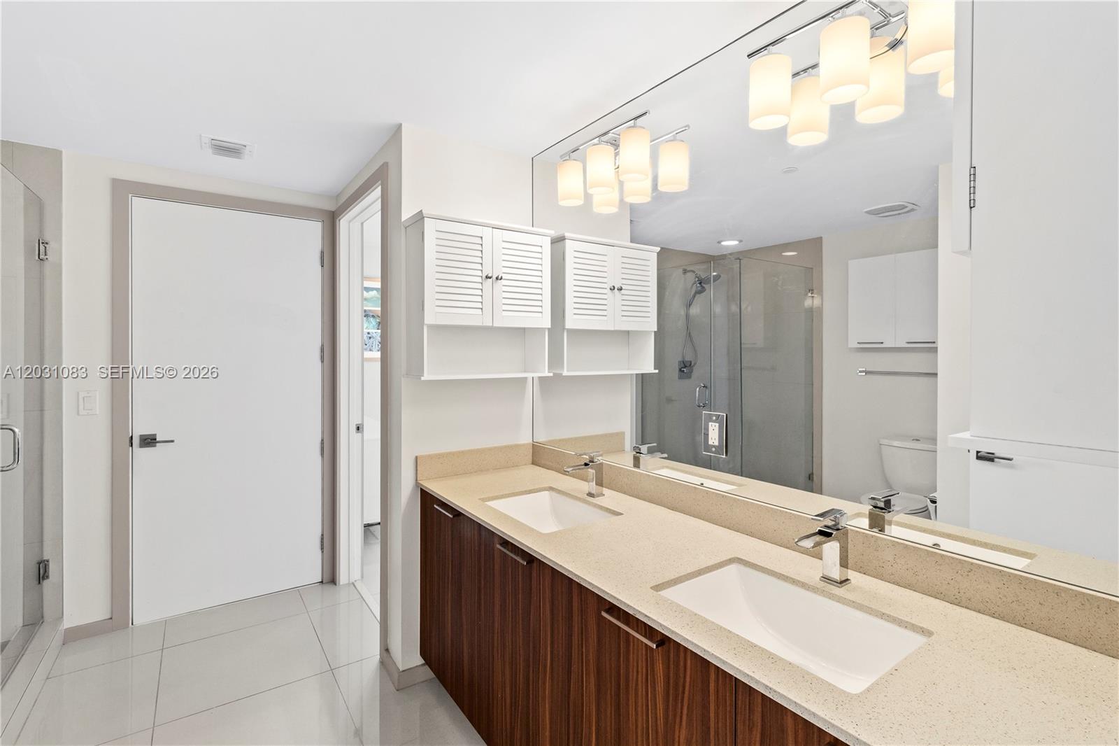A modern bathroom features a double vanity with wood cabinets, quartz countertops, and large mirrors — DORAL, FL