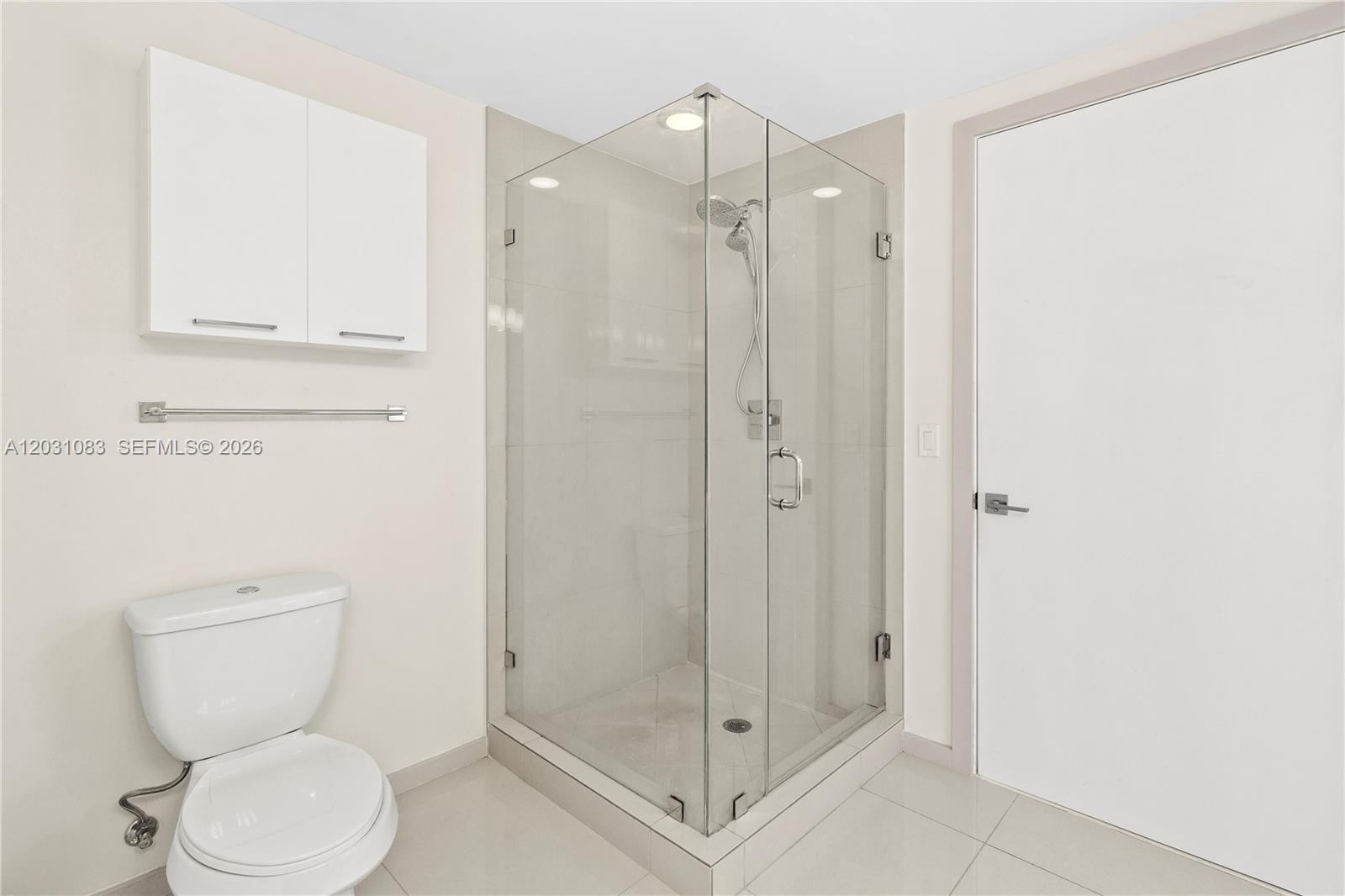 A bathroom features a white toilet, a glass-enclosed corner shower, and white wall cabinets — DORAL, FL