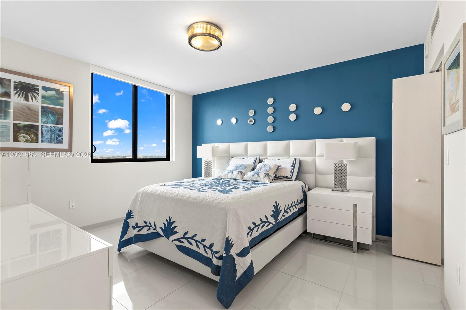 A bedroom features a blue accent wall, white furniture, and a large window with sky views — DORAL, FL