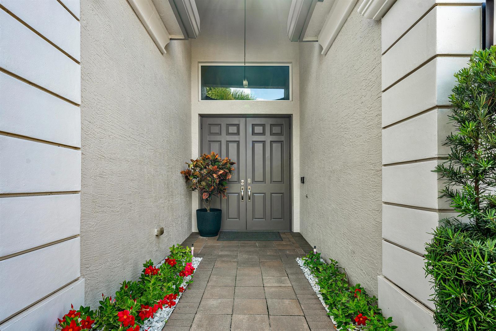 A paved walkway leads to a double front door flanked by potted plants and flowers — 12874 Granite Mountain Pass, Boynton Beach FL 33473, BOYNTON BEACH, FL