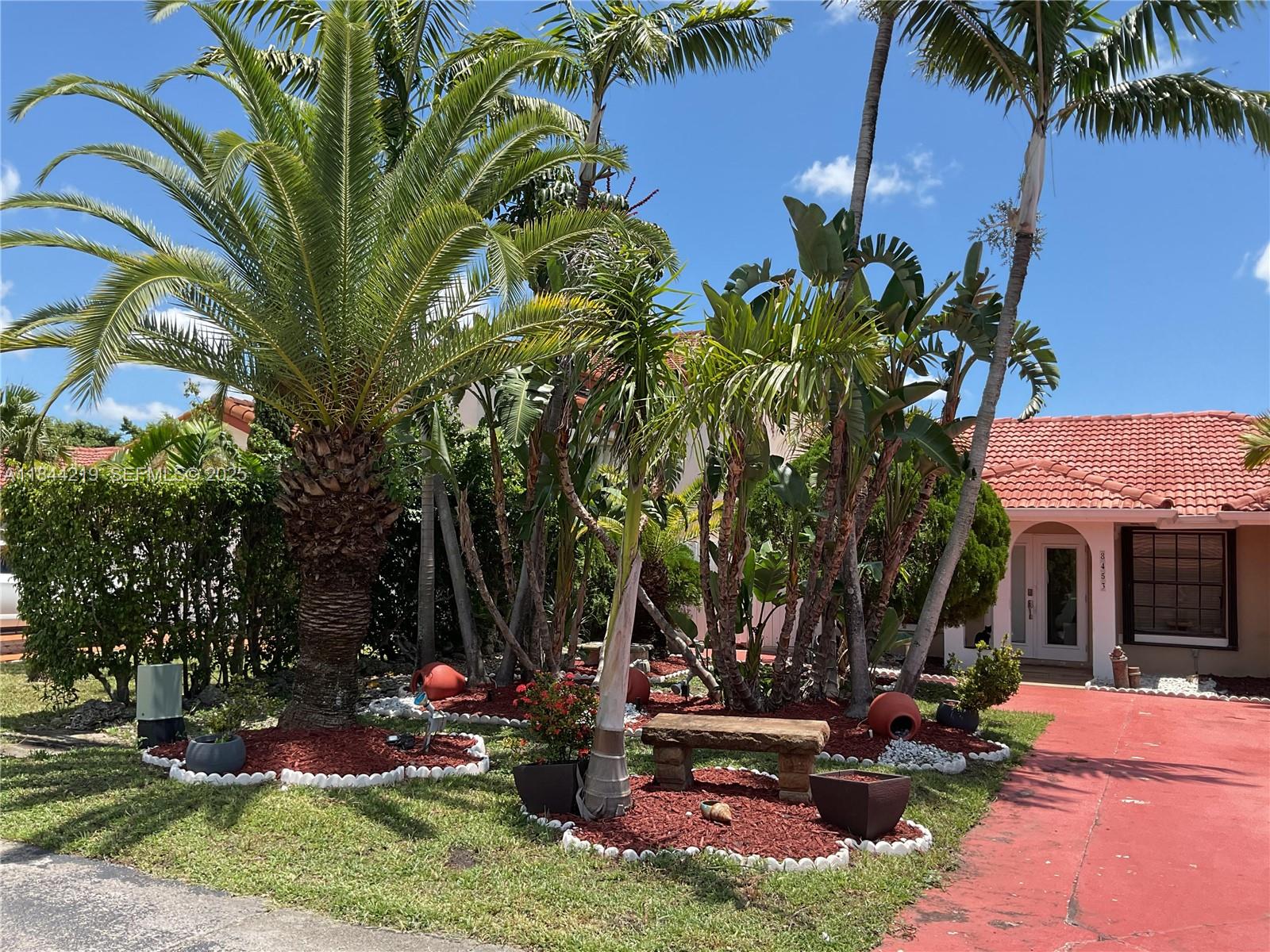 A paved entrance leads to a stucco wall with the Angelica Gardens sign and landscaping — 8453 NW 189 Street Rd, Hialeah FL 33015, HIALEAH, FL