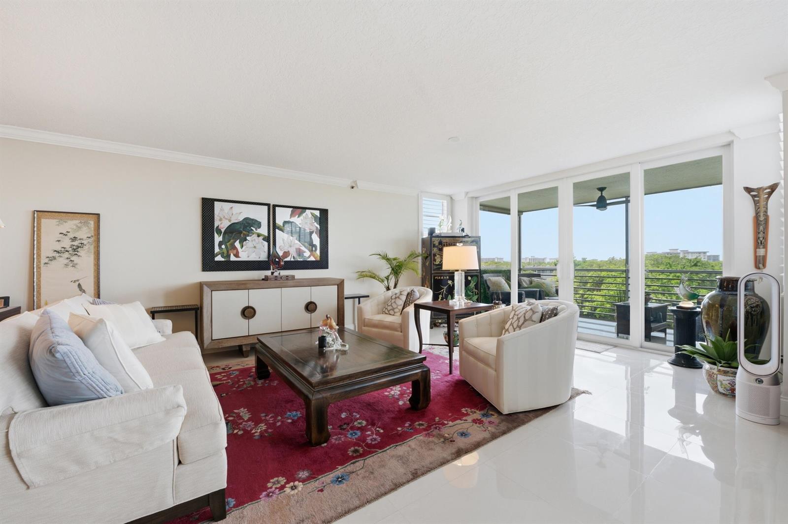 A bright living room features a magenta area rug, white furniture, and a glass balcony door — 3510 Oaks Way # 703, Pompano Beach FL 33069, POMPANO BEACH, FL