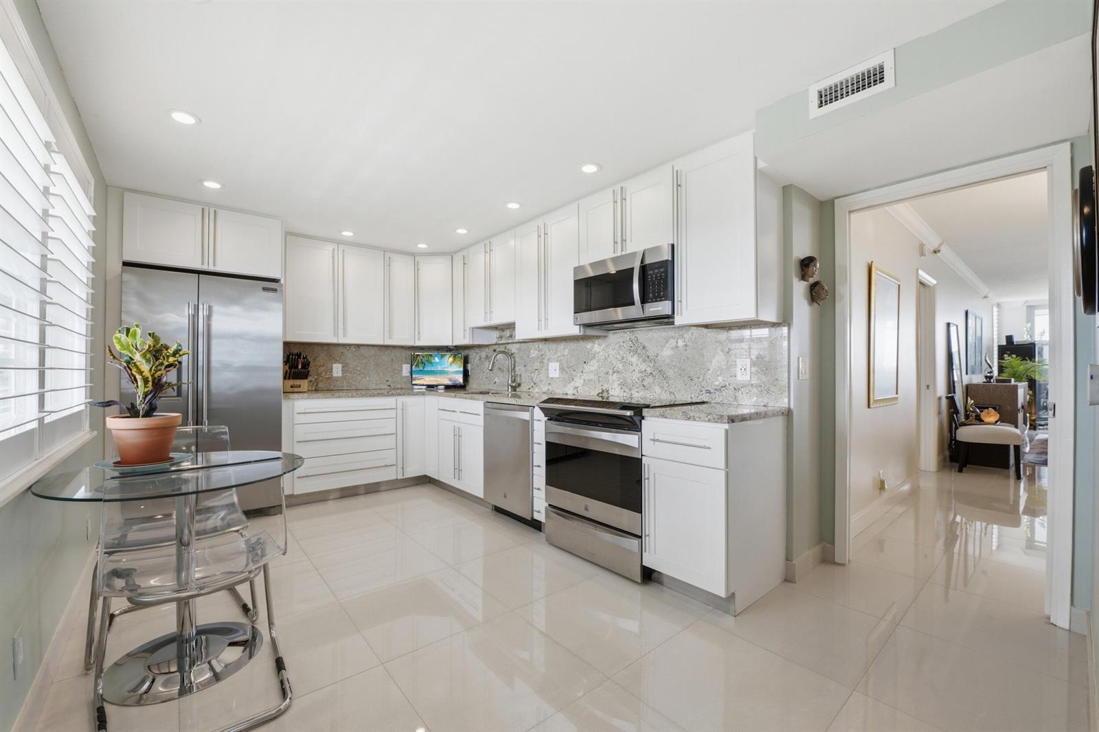 A modern kitchen features white cabinetry, stainless steel appliances, granite countertops, and a glass table — 3510 Oaks Way # 703, Pompano Beach FL 33069, POMPANO BEACH, FL
