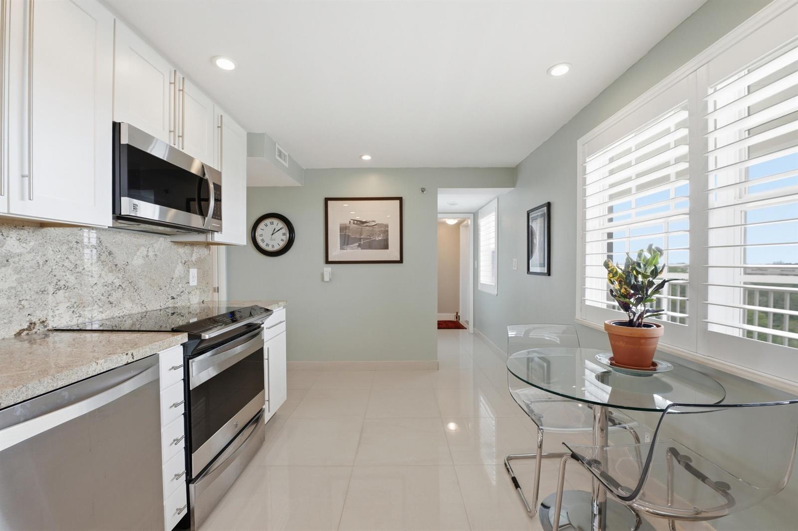A kitchen with white cabinets, stainless steel appliances, and a glass dining table by a window — 3510 Oaks Way # 703, Pompano Beach FL 33069, POMPANO BEACH, FL