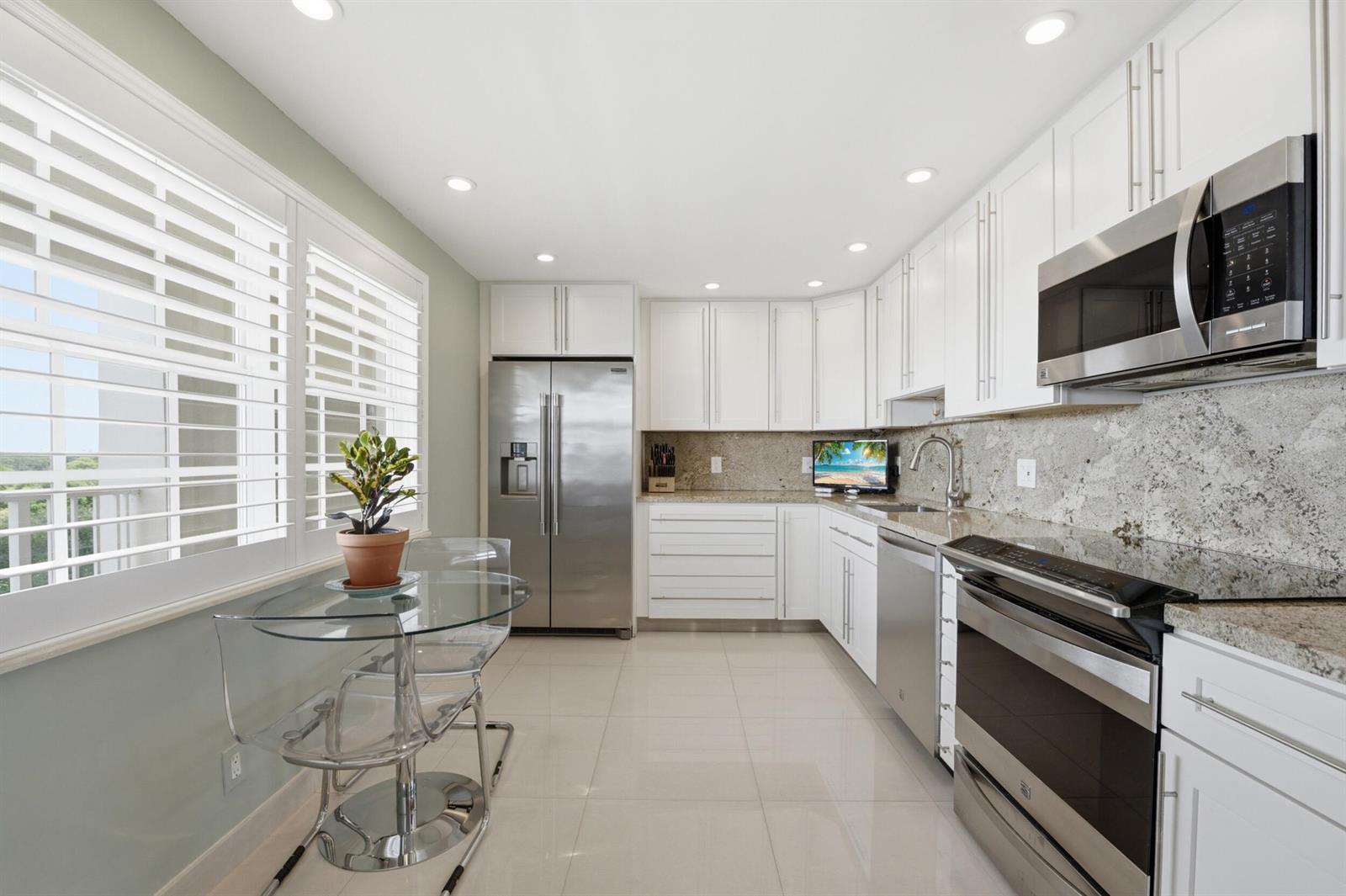 A kitchen with white cabinets, stainless steel appliances, granite countertops, and a glass dining table — 3510 Oaks Way # 703, Pompano Beach FL 33069, POMPANO BEACH, FL