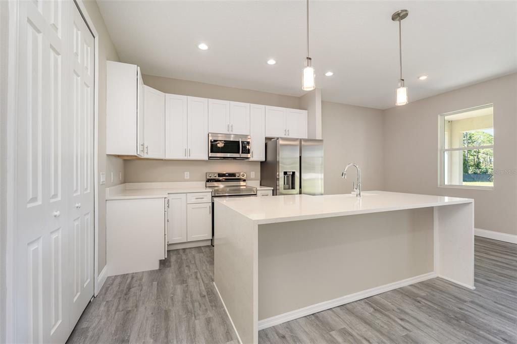 A modern kitchen features white cabinets, stainless steel appliances, a quartz island, and gray flooring — 1319 SCHNEIDER STREET SW, PALM BAY, FL