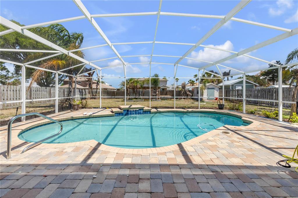 A screened-in swimming pool with a small waterfall feature and paver patio in a backyard — 10 CUNNINGHAM DRIVE, NEW SMYRNA BEACH, FL