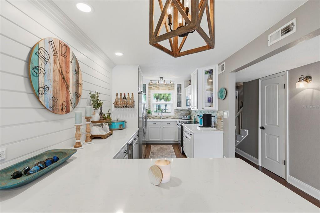 A white kitchen features a large wall clock, shiplap siding, and a wooden geometric chandelier — 4751 COQUINA KEY DRIVE SE, ST PETERSBURG, FL