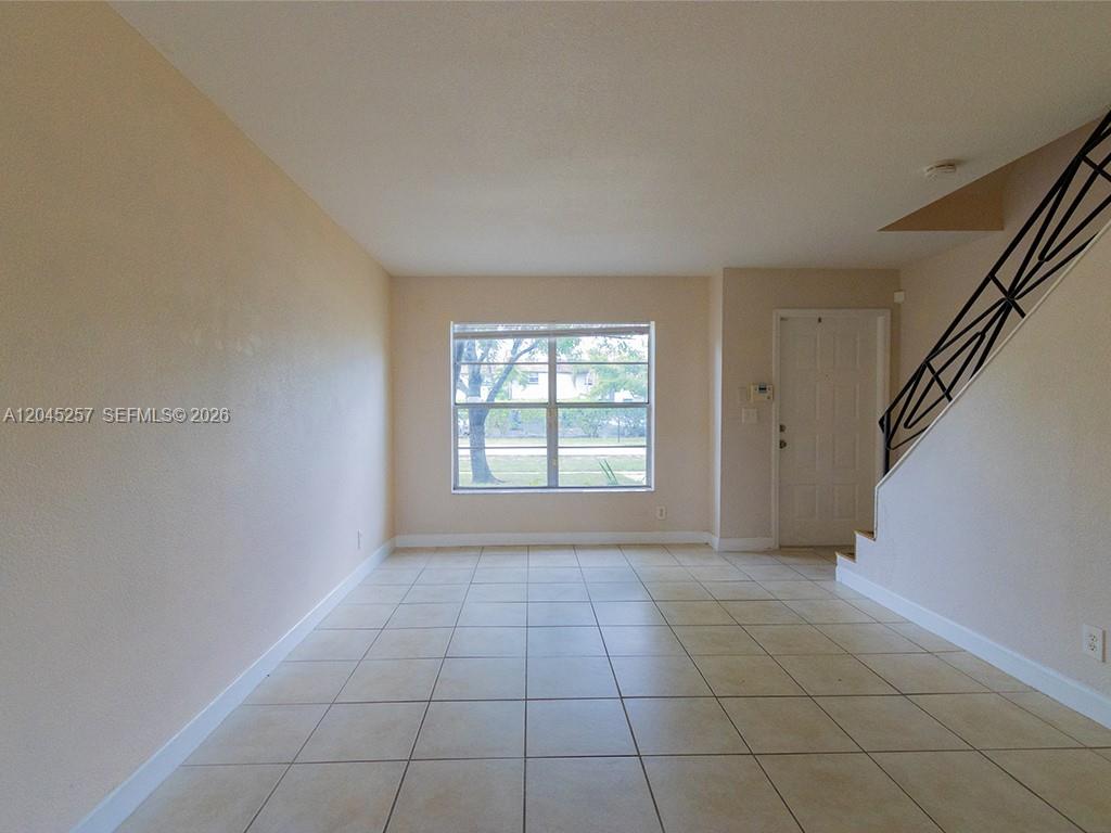 An empty room features beige tile flooring, light-colored walls, a large window, and a staircase — 4648 NW 9th Dr # 4648, Plantation FL 33317, PLANTATION, FL