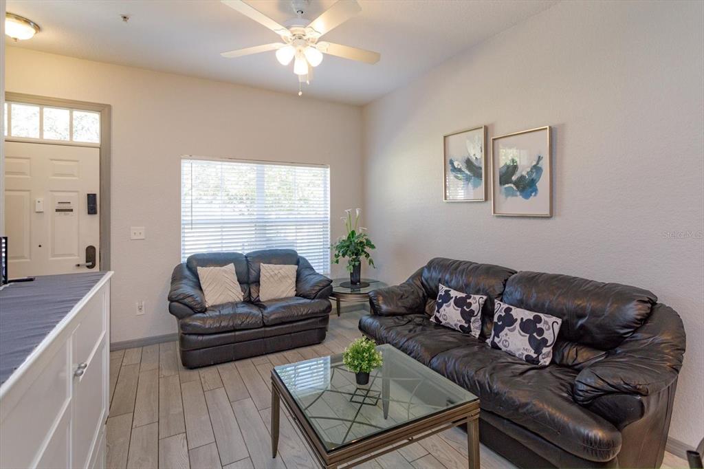 A living room features two black leather sofas, a glass coffee table, and tile flooring — 2211 SAN VITTORINO CIRCLE UNIT 103, KISSIMMEE, FL