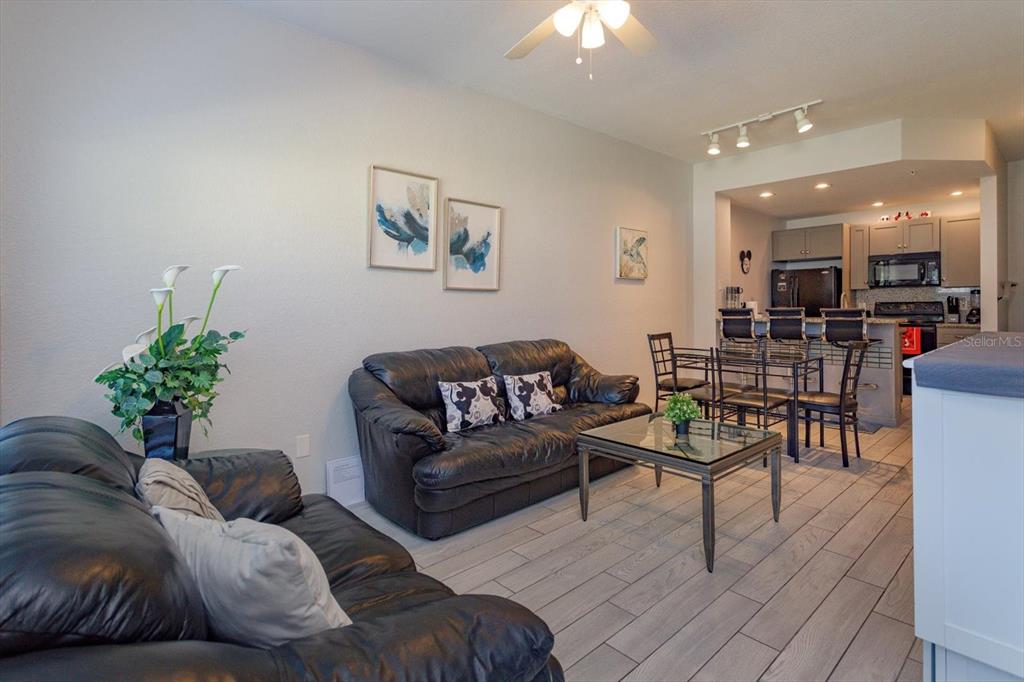 A living room with black leather sofas and a glass coffee table near a kitchen — 2211 SAN VITTORINO CIRCLE UNIT 103, KISSIMMEE, FL